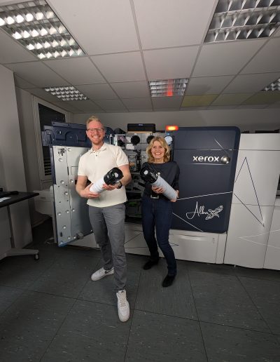 Felix Fuchs und Birgit Hermes lachend mit Tonerkartuschen vor der Xerox Iridesse